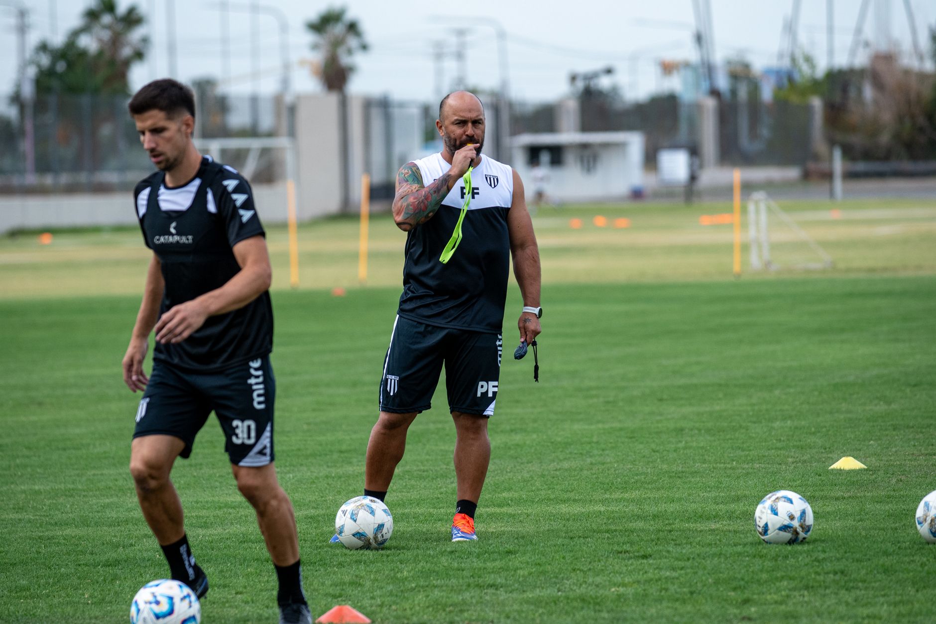 Focused soccer coach instructing players during a training session on a green field.