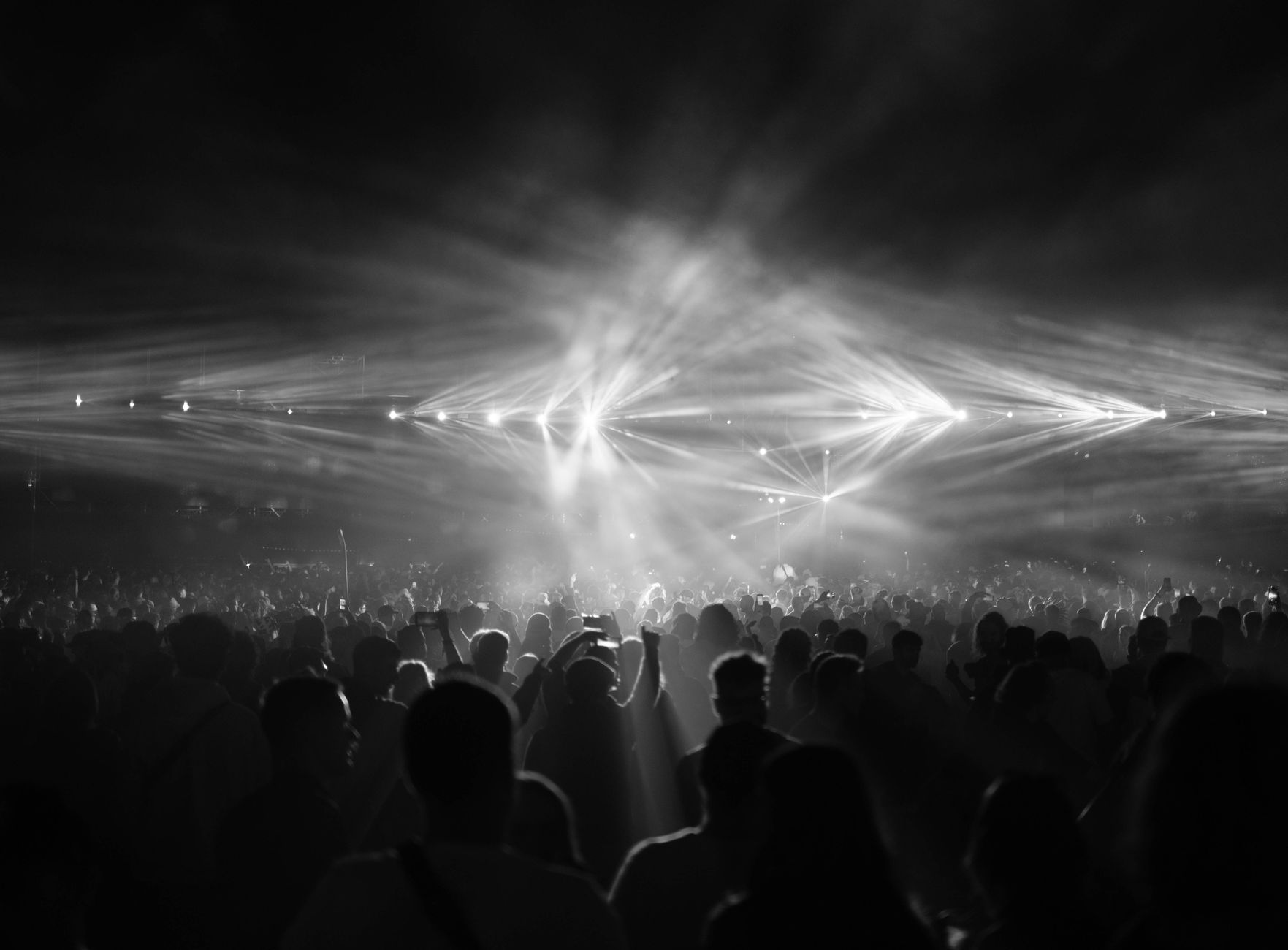 A dramatic black and white photo capturing a crowd at a night concert with bright stage lights.