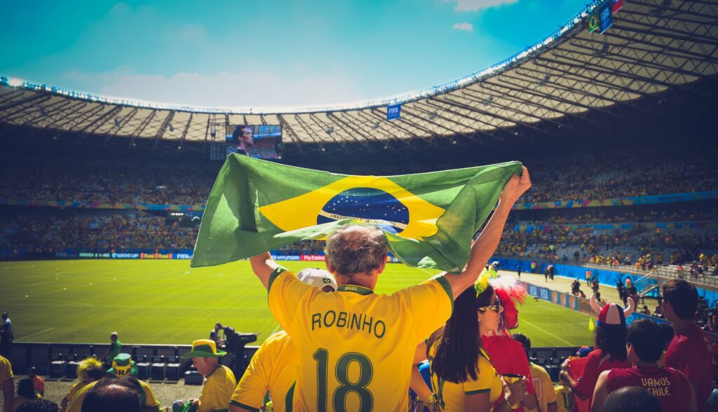 Excited Brazilian fans holding flag at soccer match in vibrant stadium atmosphere.