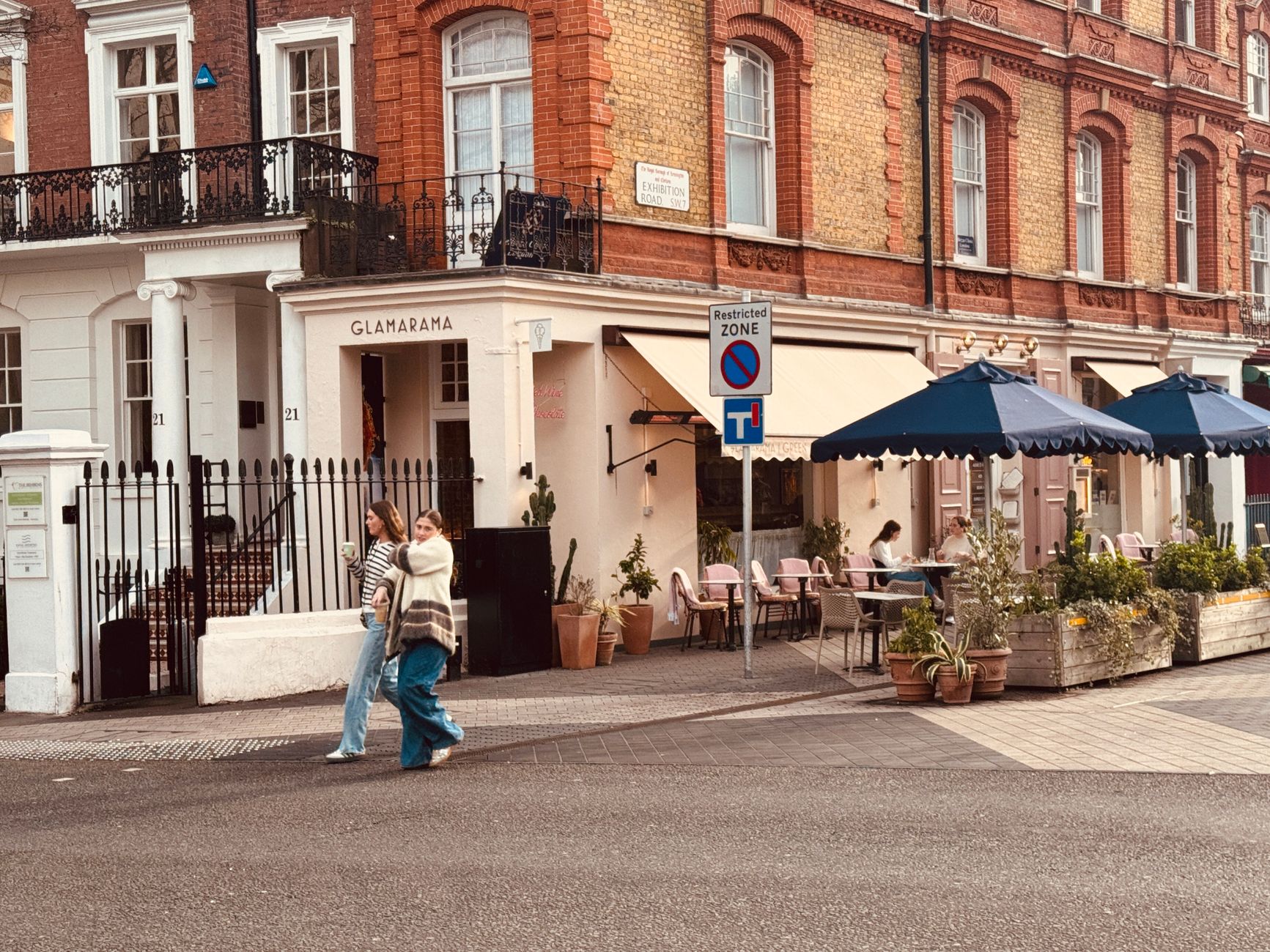 A vibrant street scene with a cafe and two women walking past colorful storefronts.
