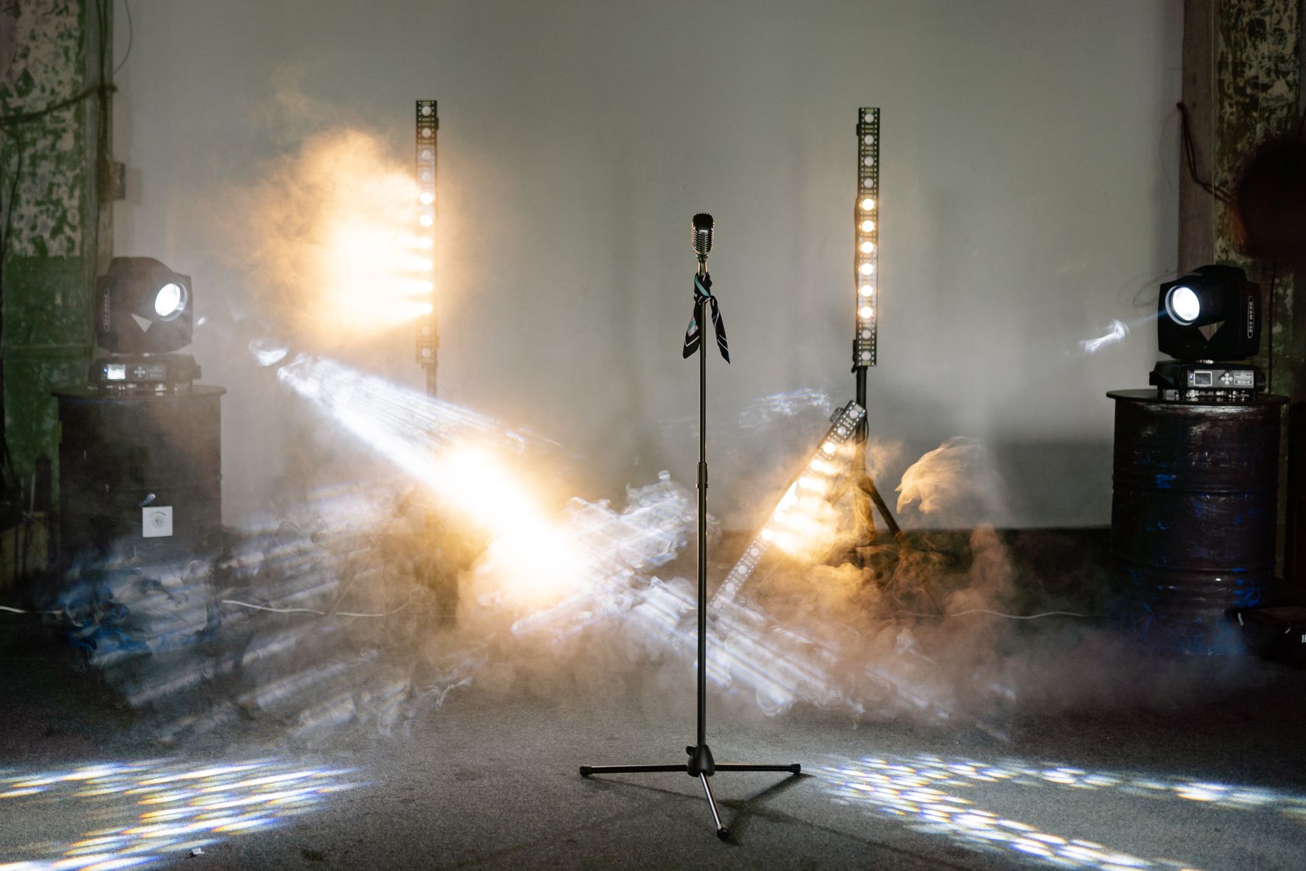 A microphone stands center stage surrounded by dramatic lights and smoke, ready for a performance.