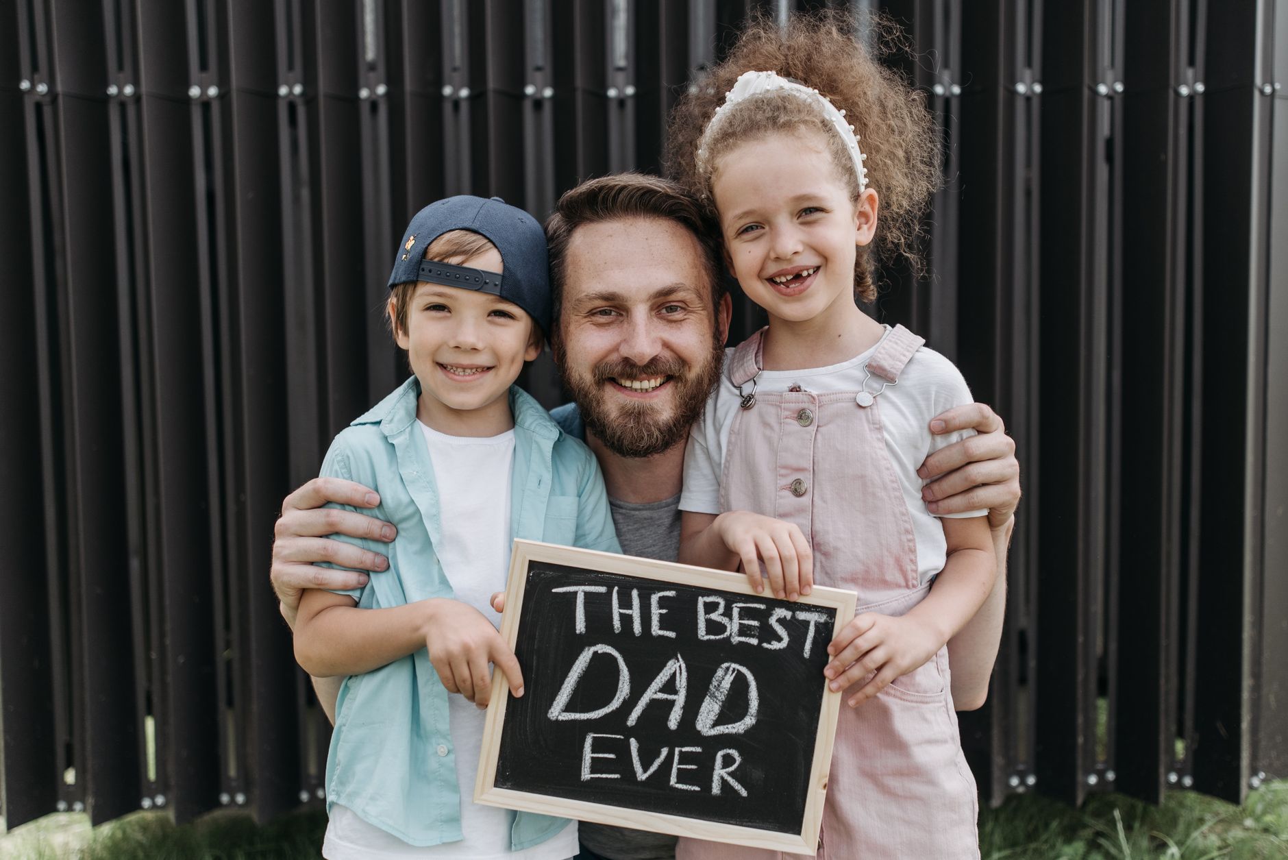 A joyful father hugging his children with a "Best Dad Ever" sign.