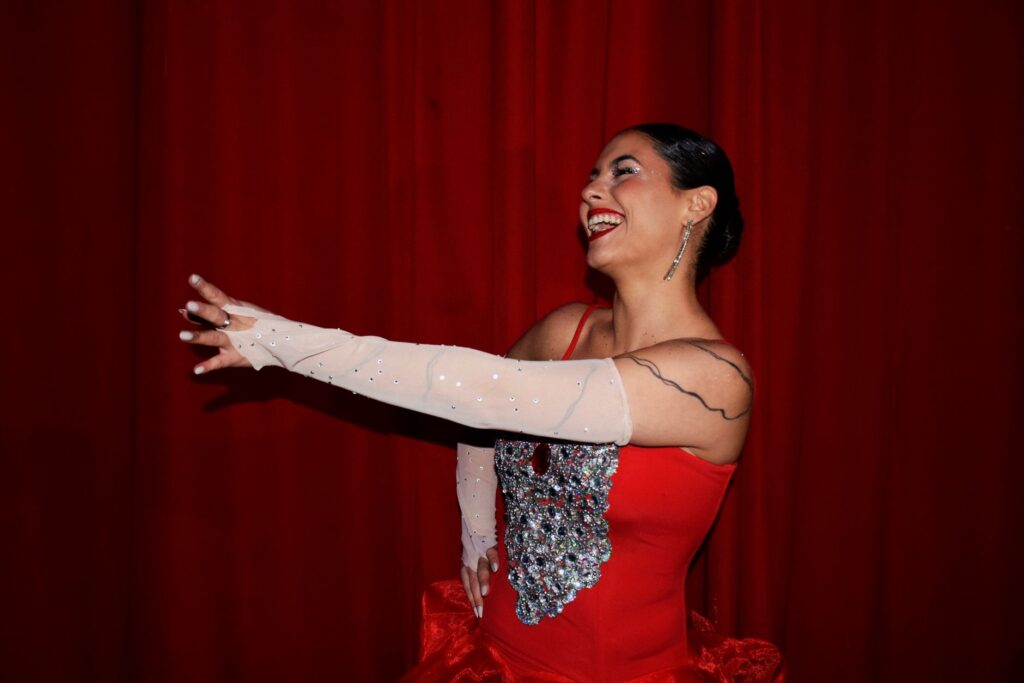 Elegant woman in a sparkling red dress performing on stage with red curtains.