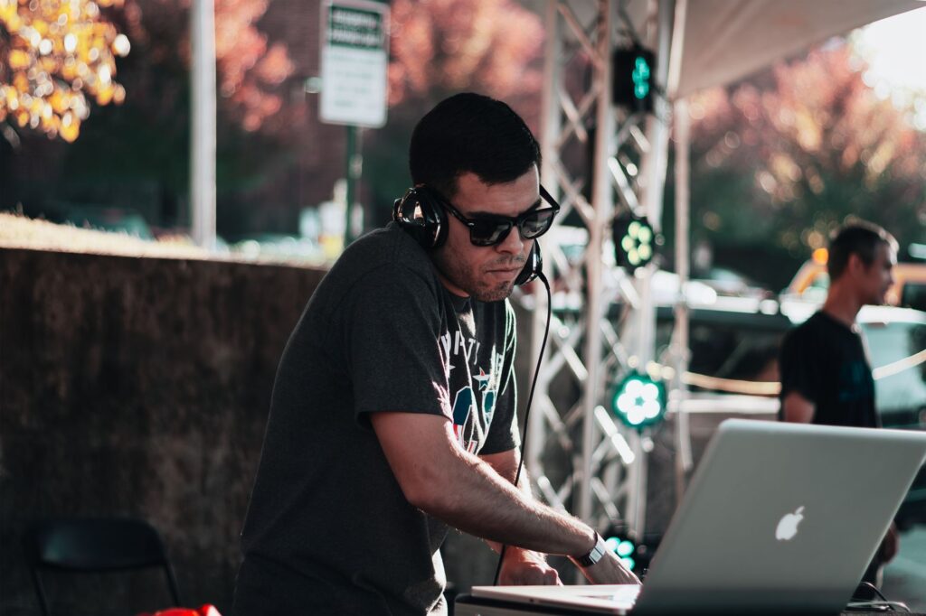 DJ performing outdoors in Fayetteville, AR using a laptop and headphones.