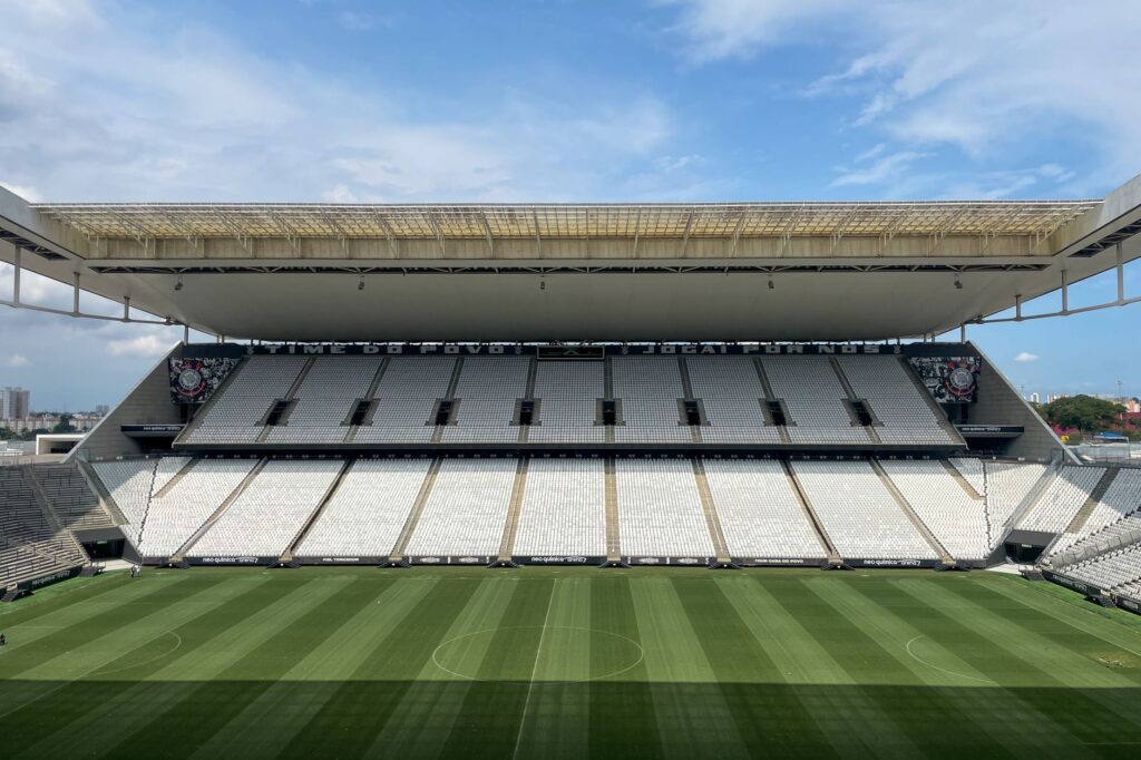 Wide view of an empty football arena in São Paulo, featuring a green pitch under a sunny sky.