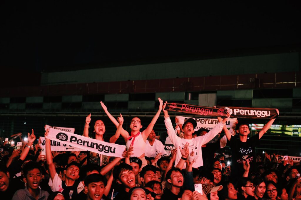 Vibrant crowd cheering at an outdoor nighttime concert holding banner.