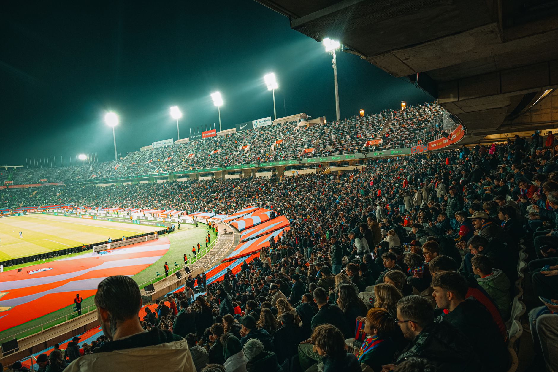 A vibrant nighttime soccer match with a packed stadium full of enthusiastic fans.