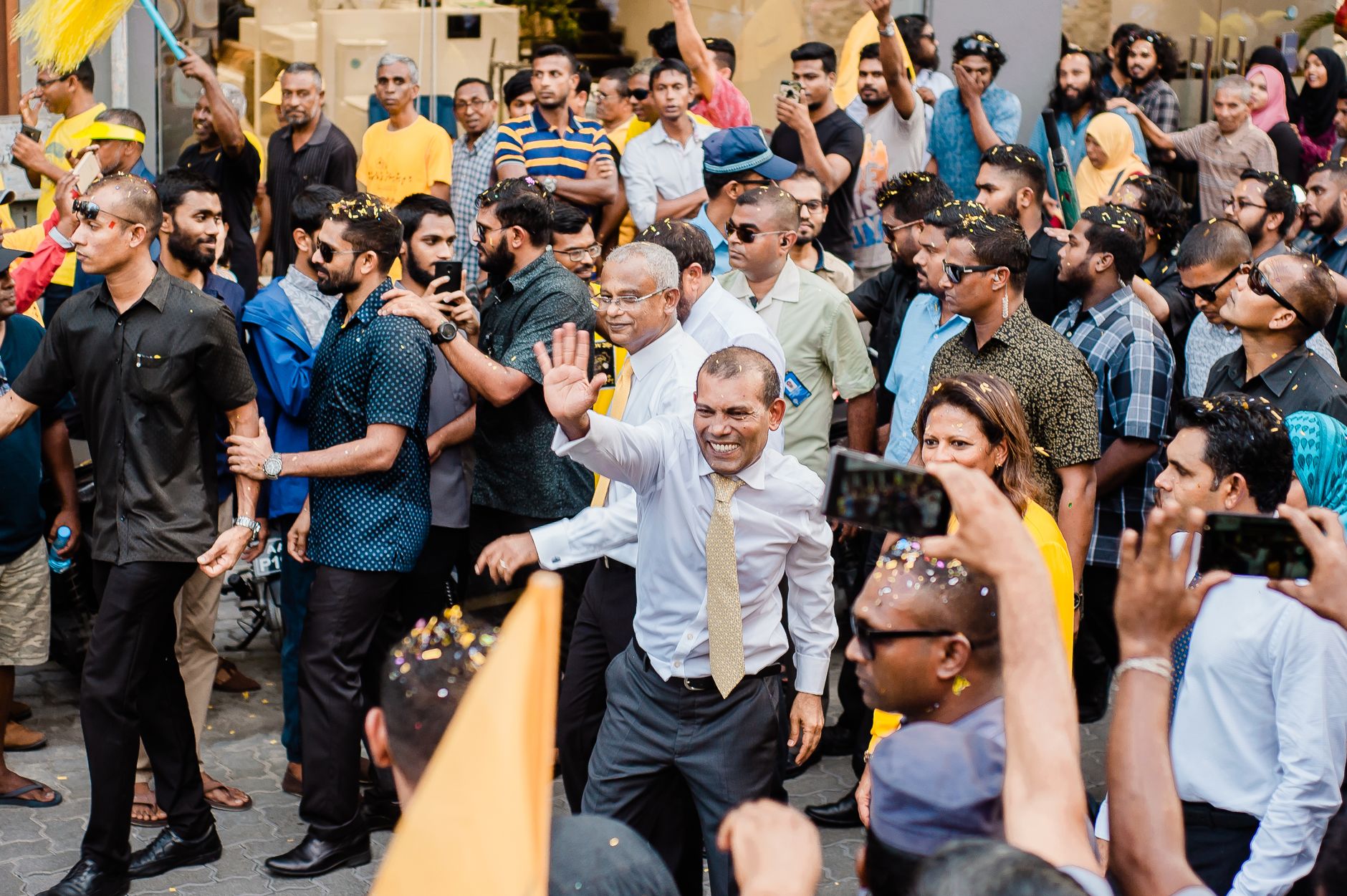 A politician waves to a crowd during a lively outdoor rally in a city street.