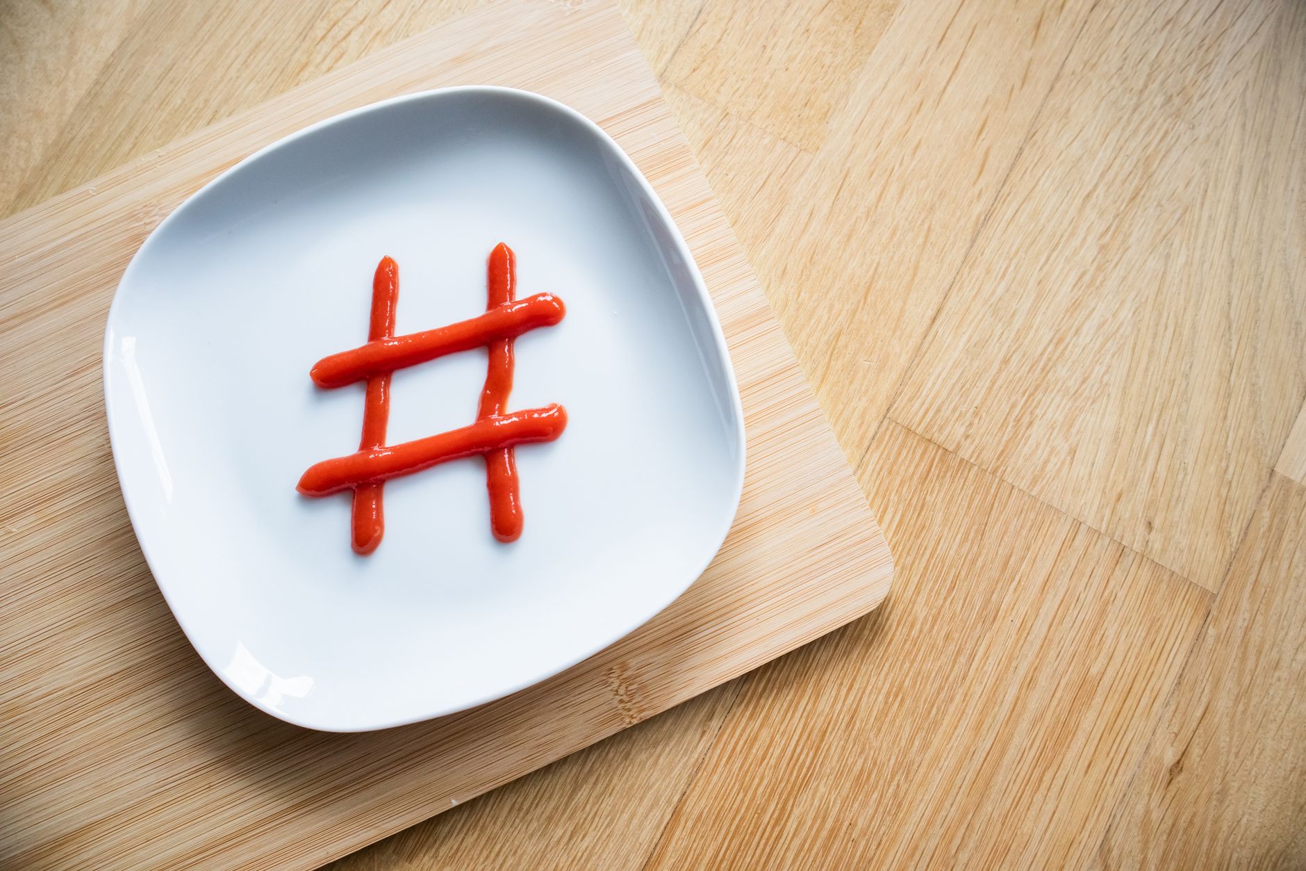 Ketchup arranged as a hashtag on a white plate on wooden surface, shot from above.