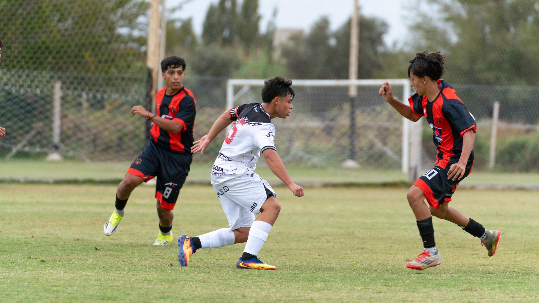 Three youth soccer players in action during an outdoor match on a green field.