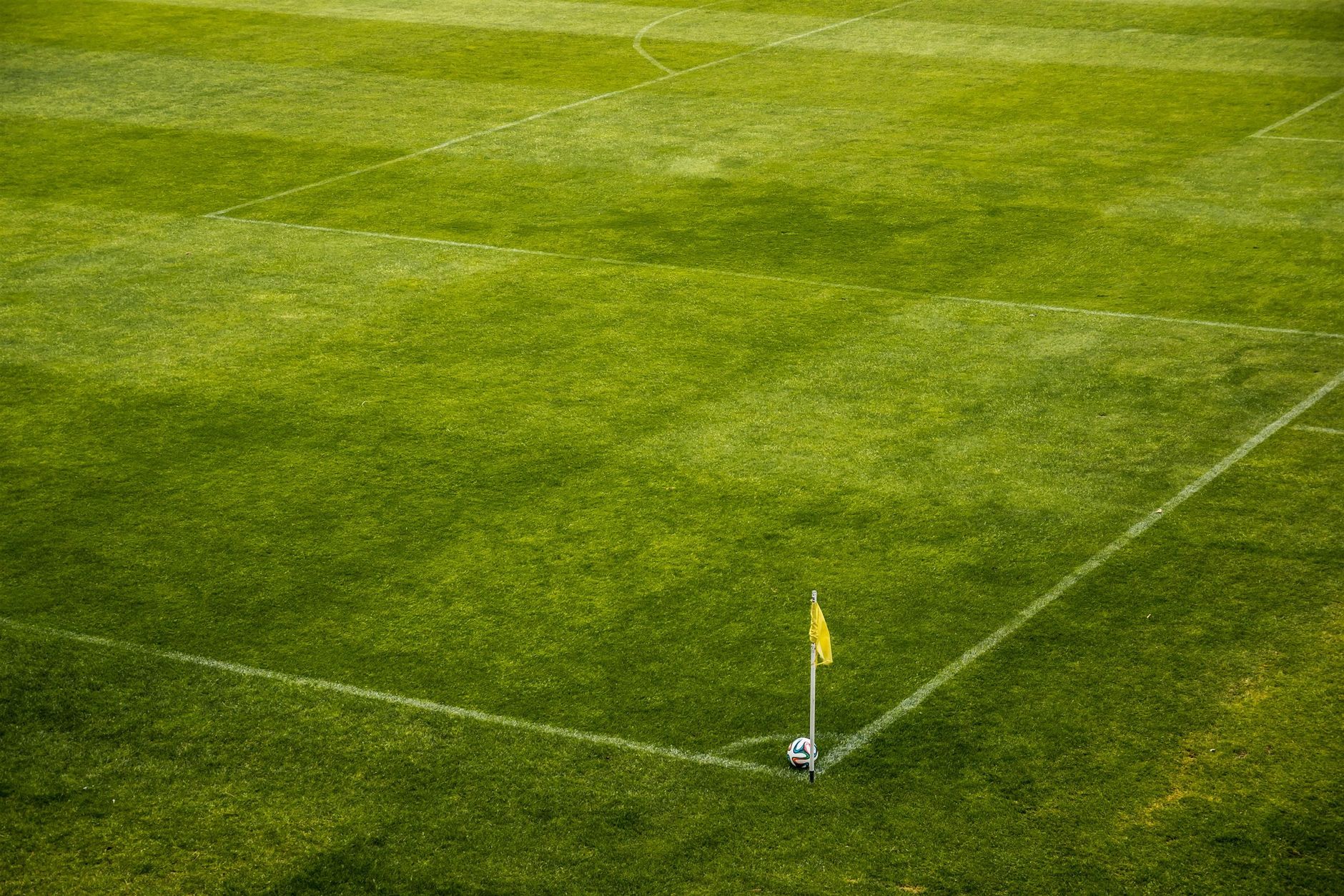 A vibrant green soccer field corner with a yellow flag and soccer ball, perfect for sports themes.