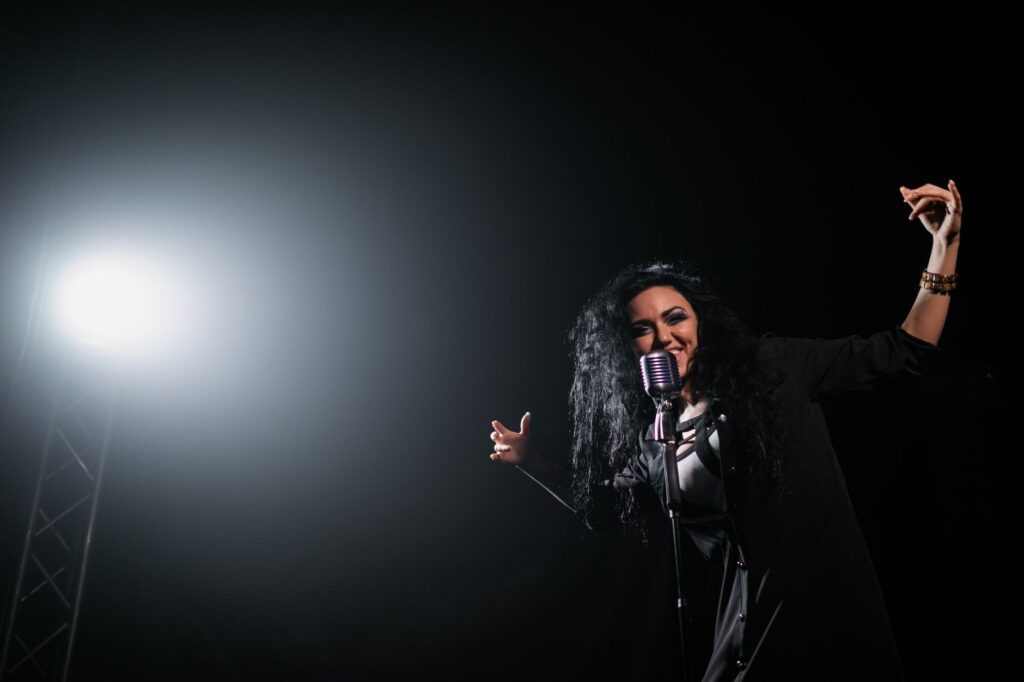 A vibrant female singer passionately performing under a spotlight on stage.